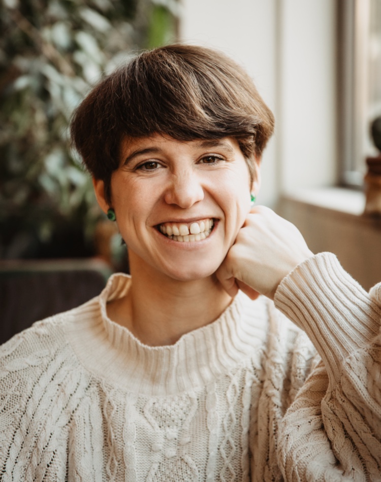 Nahaufnahme von Clara Fohrbeck in Boulderhalle in Berlin Kreuzberg, die für Therapeutisches Klettern und Systemisches Coaching in die Kamera lächelt.